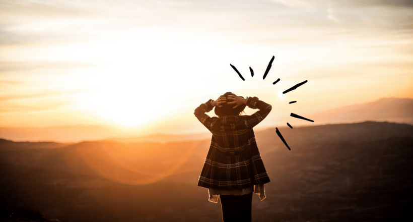 Person von hinten fotografiert vor einem Sonnenuntergang. Die Person blickt auf eine weite Landschaft im Licht des Sonnenuntergangs.