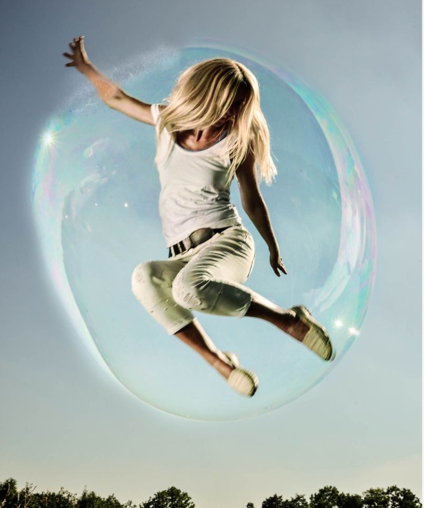 A blonde woman jumping in the air inside a large, transparent bubble