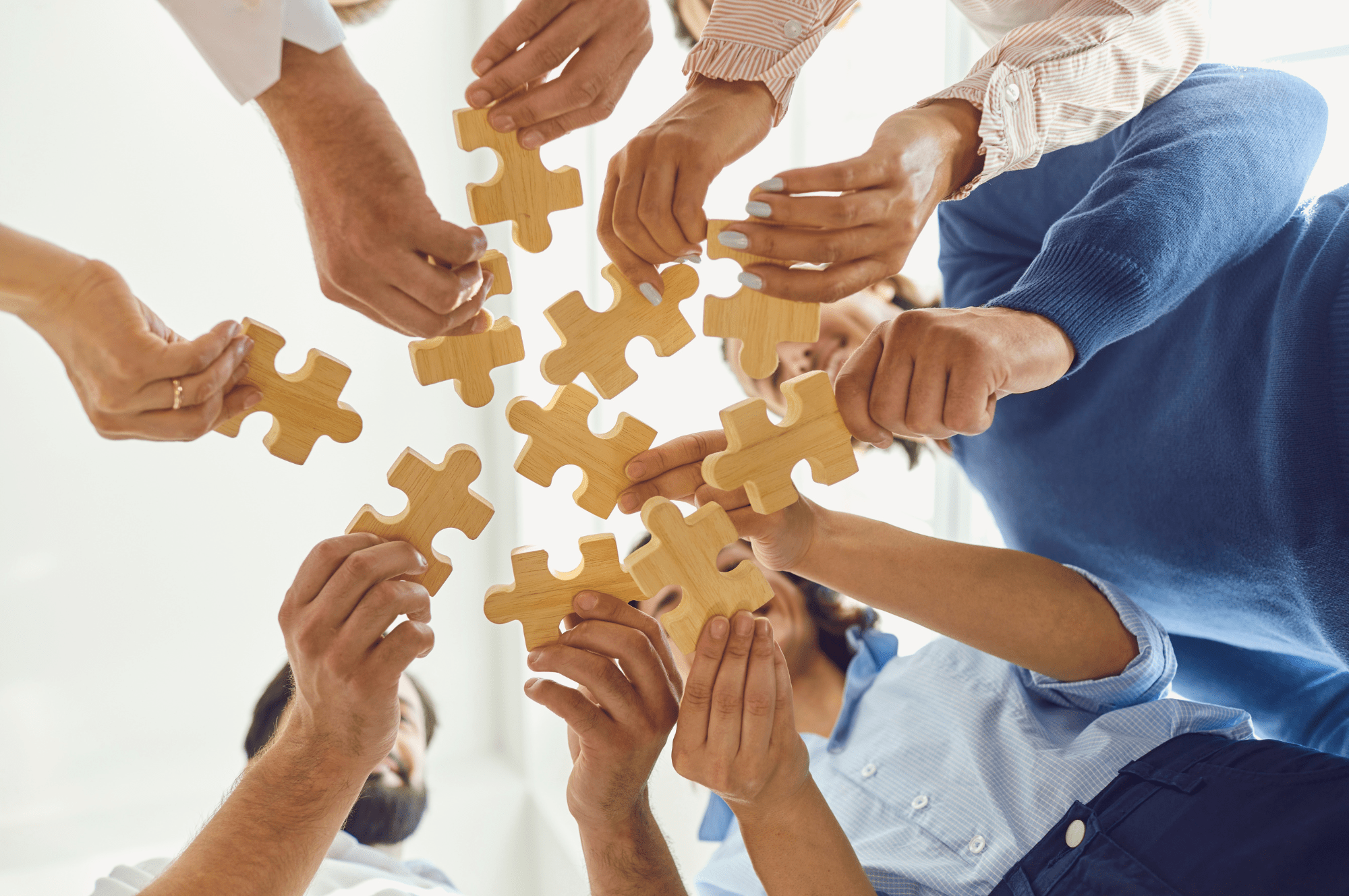 Various hands holding wooden puzzle pieces, symbolizing teamwork and collaboration